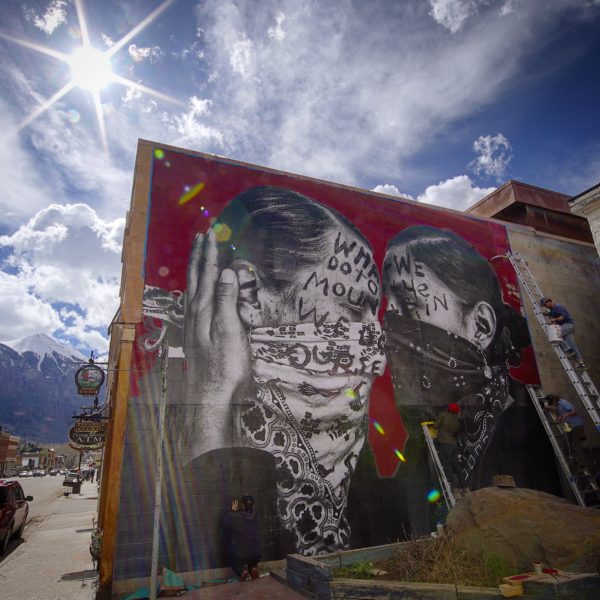 Chip Thomas, aka jetsonorama, (in the red hat) puts the finishing touches on his main street mural on Sunday. [Photo by Jim Hurst]