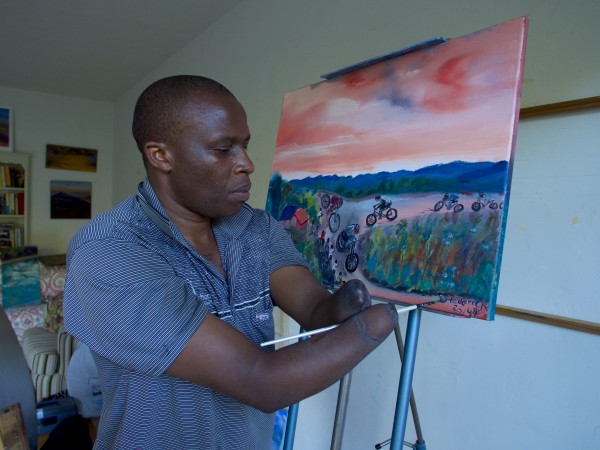 Frederick Ndabaramiye painting. At 15, his hands were cut off by militants. Now he rides a bike, paints and enables other who believe they are disabled.